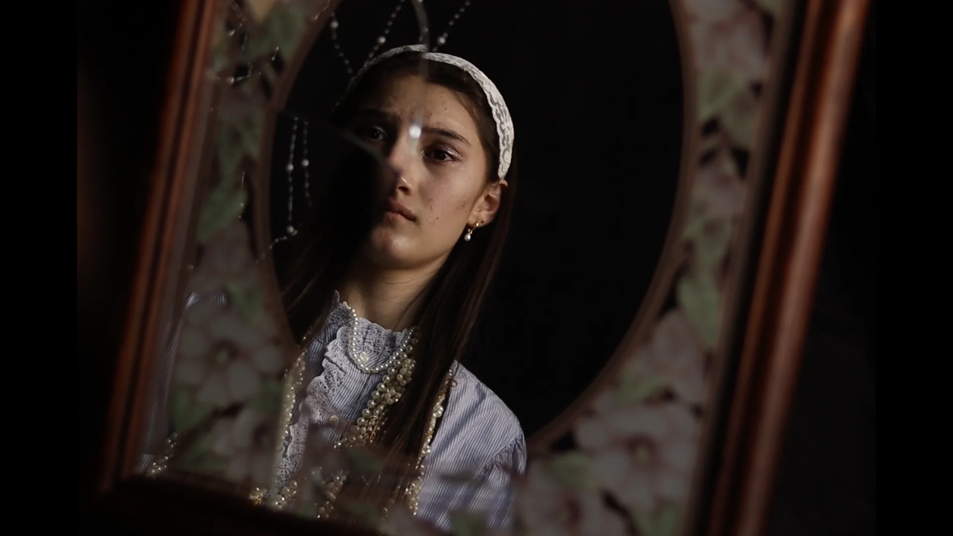 A young woman reflected in an ornate mirror, a still from Sophia's film work.